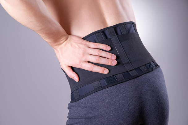 Man with a medical belt for the back on a gray background, studio shot - Fotografie, Obrázek