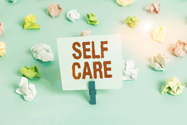 Text sign showing Self Care. Conceptual photo practice of taking action to preserve or improve ones own health Colored crumpled papers empty reminder blue floor background clothespin. - Photo, Image