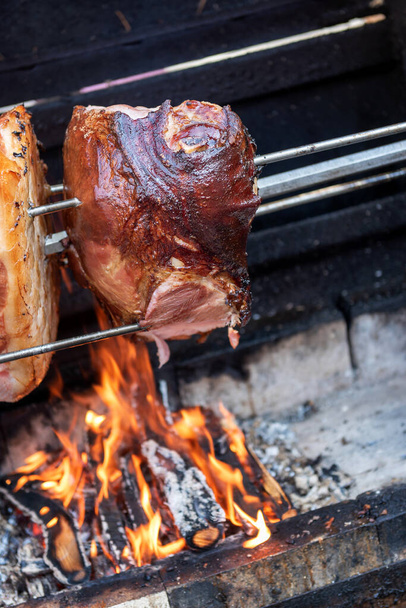 Targ, uliczne jedzenie, festiwal jedzenia. Gotowanie dużego kawałka wieprzowiny na otwartym ogniu. Wschodnioeuropejskie tradycje. Koncepcja żywności. - Zdjęcie, obraz