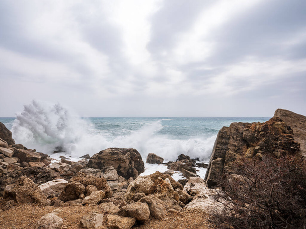 Olas golpeando rocas en la costa de Baunei. Fondo borroso y con luz solar filtrándose de las nubes. Fondo natural dramático
. - Foto, Imagen