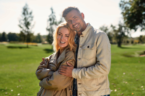 In love. Portrait of romantic couple hugging and smiling while standing in the middle of the beautiful park - Фото, изображение
