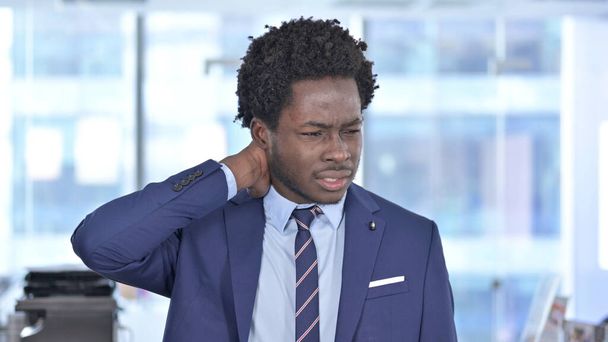 オフィスで首の痛みを持つアフリカ系アメリカ人ビジネスマンの疲れ - 写真・画像