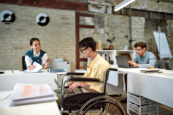 Sharing Energy, Ideas, and Space. Guy in a wheelchair working in the office - Photo, Image