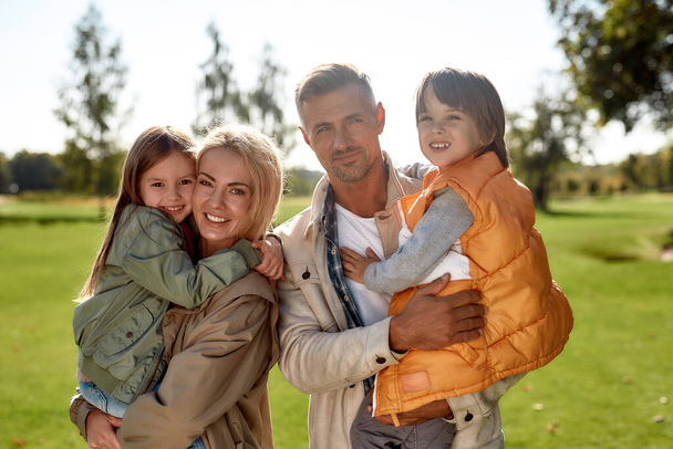 Spending time together. Portrait of happy and beautiful family looking at camera with smile while standing in the park on a sunny day - Foto, Imagem