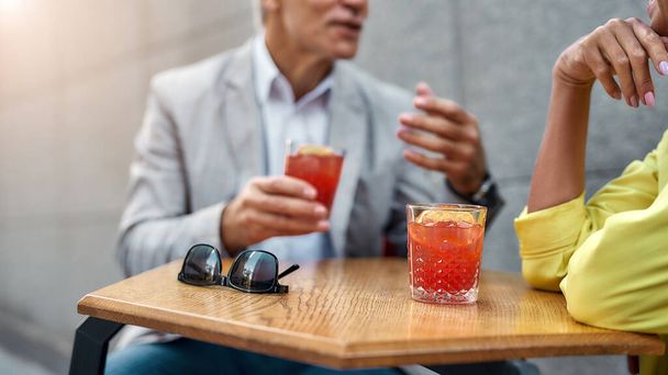 Cropped photo of stylish people drinking cocktails and discussing something while sitting in cafe outdoors together - Photo, image