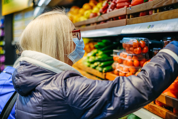 Стара жінка в медичних масках купує в супермаркеті, шукаючи їжу
 - Фото, зображення