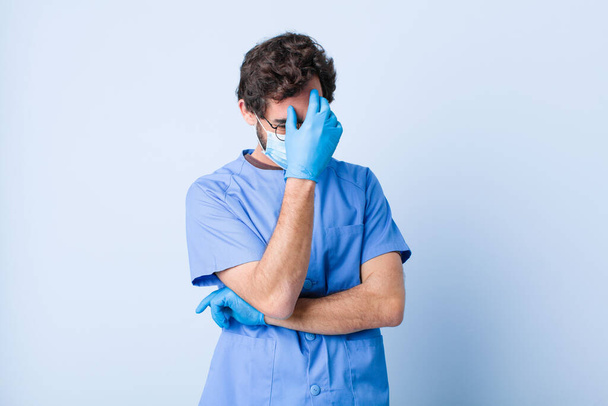 молодий чоловік, дивлячись на стрес, соромно або засмучений, з головним болем, покриває обличчя рукою. концепція коронавірусу
 - Фото, зображення
