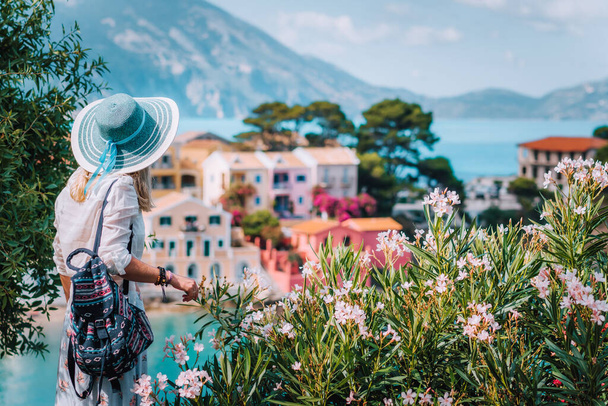 Блондинки-туристки носят солнечную шляпу, наслаждаясь красивой яркой и красочной деревней Assos на острове Кефалония, Греция
 - Фото, изображение