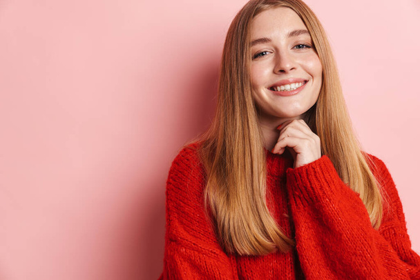 Photo of happy beautiful woman in red sweater smiling and looking at camera isolated over pink wall - Fotó, kép