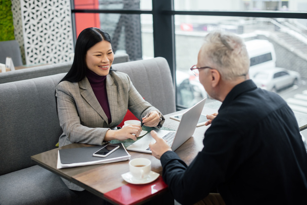 enfoque selectivo de sonriente mujer de negocios asiática hablando con hombre de negocios durante reunión de negocios
  - Foto, imagen