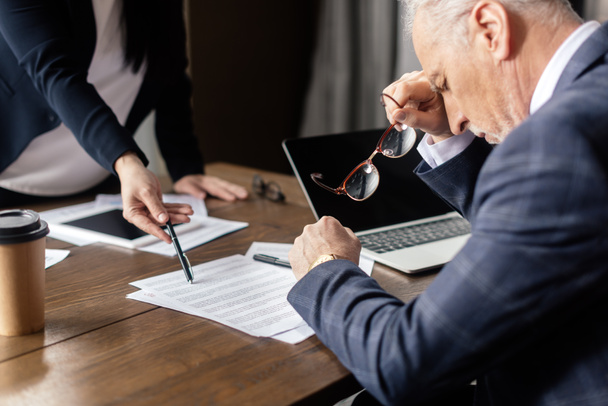 καλλιεργημένη άποψη της επιχειρηματία δείχνοντας σε χαρτιά και επιχειρηματία κρατώντας γυαλιά κατά τη διάρκεια της επαγγελματικής συνάντησης  - Φωτογραφία, εικόνα