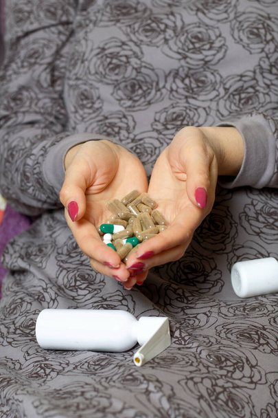 A woman sits on a bed and holds a handful of pills in her palms. Protection against infection in self-isolation during coronavirus. - Photo, Image