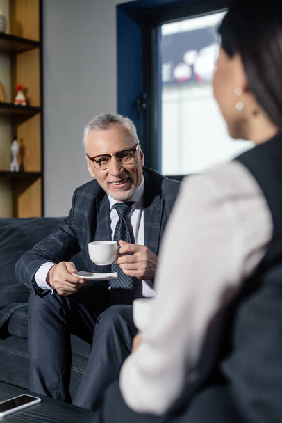 selective focus of smiling businessman holding cup and talking with businesswoman  - Foto, imagen