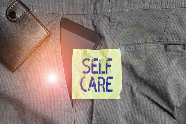 Käsiala teksti kirjallisesti Self Care. Käsitteellä tarkoitetaan käytäntöä ryhtyä toimiin oman terveyden säilyttämiseksi tai parantamiseksi Älypuhelin laite housujen sisällä etutasku lompakolla ja muistiinpanopaperilla
. - Valokuva, kuva