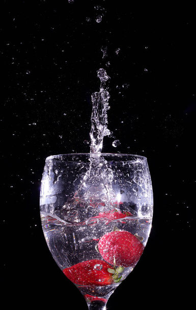 Un par de fresas cayendo en un vaso lleno de licor, también viendo gotas de salpicaduras
 - Foto, imagen