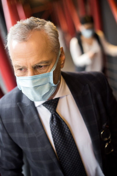 zakenman in formele kleding met medisch masker kijken weg  - Foto, afbeelding