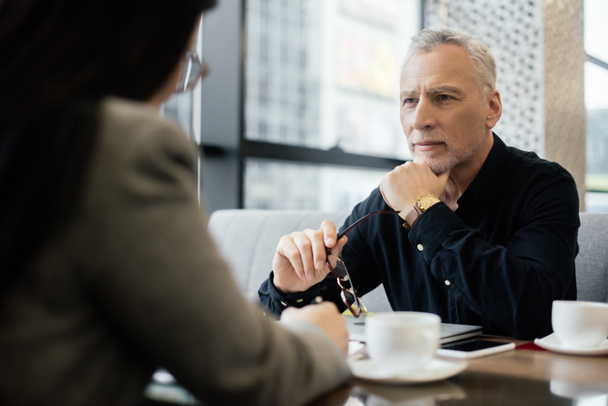 enfoque selectivo de hombre de negocios sosteniendo gafas y hablando con la mujer de negocios en la cafetería
  - Foto, Imagen