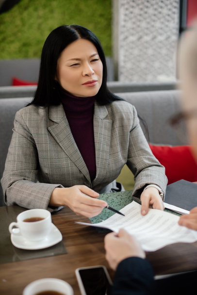 selektiver Fokus einer asiatischen Geschäftsfrau, die mit einem Geschäftsmann spricht und im Café Papiere hält  - Foto, Bild