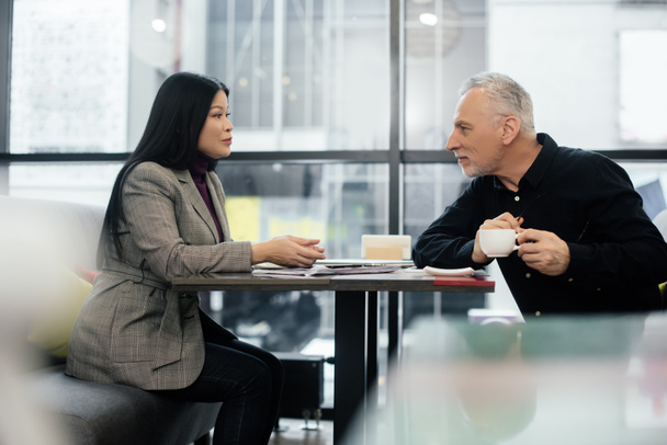 vista lateral de empresário e asiático empresária falando no café
  - Foto, Imagem