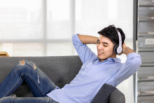 Giovane attraente asiatico uomo è sdraiato mentre ascolta la musica
. - Foto, immagini