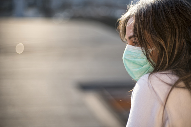 Ιός Κορόνα. Άρρωστη γυναίκα από τον ιό του στέμματος κοιτάζοντας από το παράθυρο και φορώντας προστασία αναπνοής και ανάρρωση από την ασθένεια στο σπίτι. Ασθενής απομονωμένος για πρόληψη λοίμωξης - Φωτογραφία, εικόνα