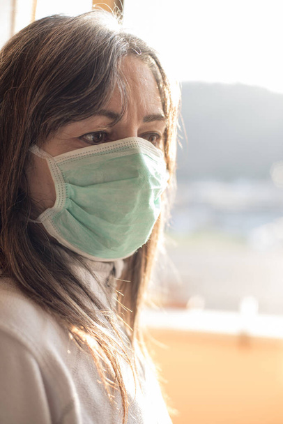 コロナウイルスだ。窓から見るコロナウイルスの病気の女性と自宅で病気からの安全呼吸保護と回復を身に着けています。感染を防ぐために隔離された患者 - 写真・画像