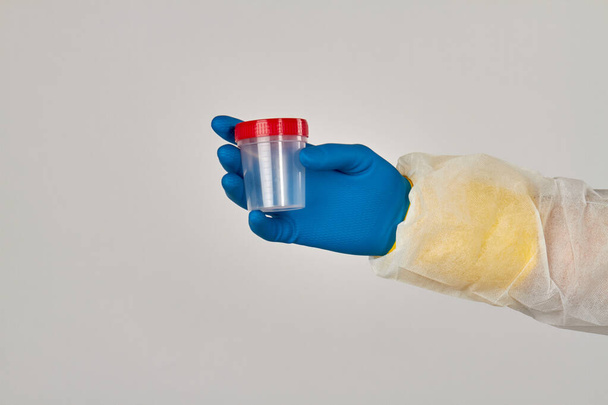 Guante azul de mano sosteniendo un recipiente vacío para análisis
. - Foto, imagen