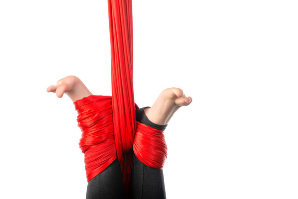Close-up of a little girl's legs tied in a knot of red airy ribbons on a white background. Concept of aerial acrobatics and sporting achievements. Advertising space - Foto, imagen