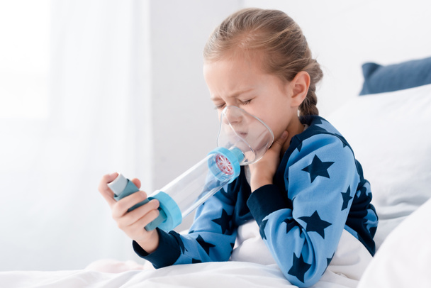 sick child with closed eyes using inhaler with spacer - 写真・画像