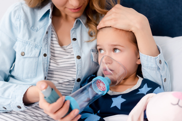 Fürsorgliche Mutter hält Inhalator mit Abstandhalter in der Nähe kranker Tochter  - Foto, Bild
