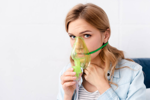 астматичная женщина, держащая респираторную маску возле лица и смотрящая в камеру
 - Фото, изображение