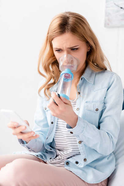 wybiórcze skupienie astmatycznej kobiety trzymającej inhalator z dystansem i smartfonem  - Zdjęcie, obraz