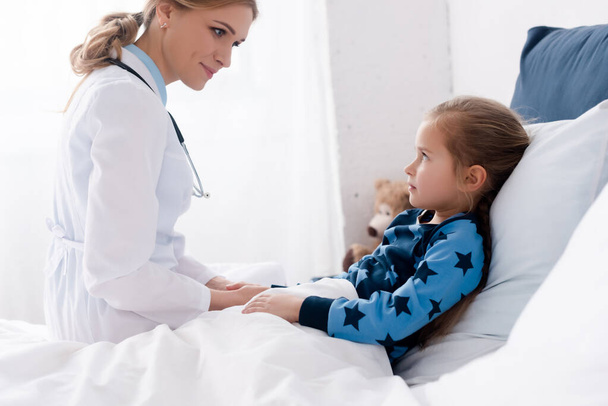 attractive doctor in white coat looking at sick kid  - Фото, зображення