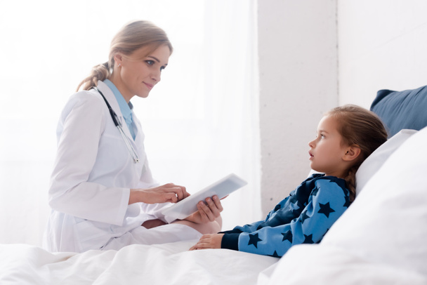 beautiful doctor in white coat using digital tablet near sick kid  - Foto, imagen