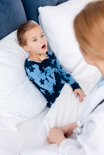 selective focus of sick kid with opened mouth touching neck near doctor  - Zdjęcie, obraz