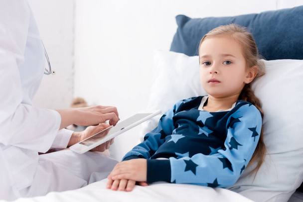 doctor in white coat holding digital tablet near sick kid  - Foto, Imagem