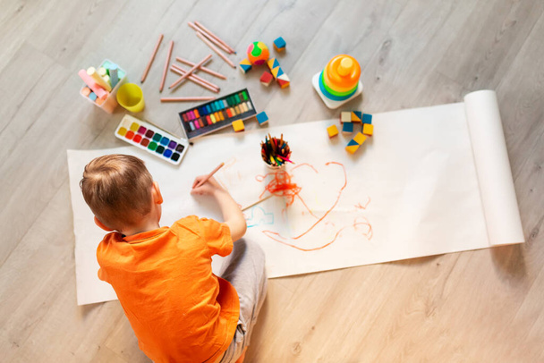 Little boy drawing a picture on the floor in his room, top view. Children's art and creativeness concept - Zdjęcie, obraz