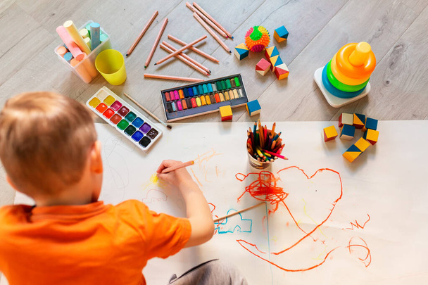 Mały chłopiec narysował obrazek na podłodze w swoim pokoju, widok z góry. Koncepcja sztuki i kreatywności dzieci - Zdjęcie, obraz