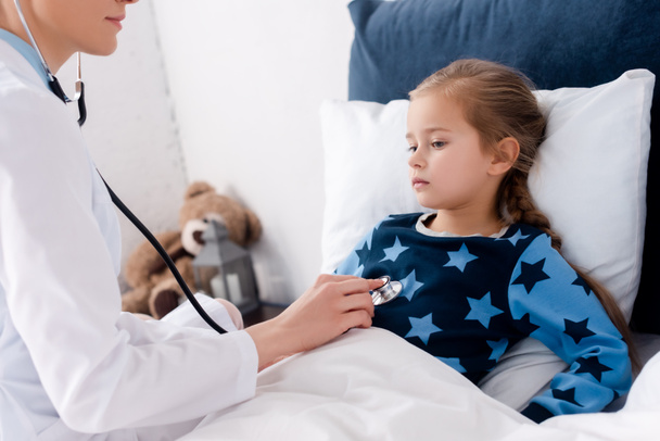doctor with stethoscope examining sick child in bedroom  - Foto, Imagem