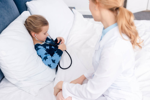 selective focus of sick kid holding stethoscope near doctor  - Foto, afbeelding