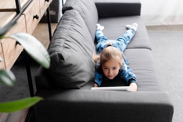 ソファに横になってデジタルタブレットを使ってかわいい子供の選択的な焦点 - 写真・画像