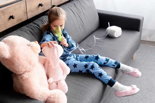 astmatische kind met behulp van compressor inhalator in de buurt van zacht speelgoed  - Foto, afbeelding