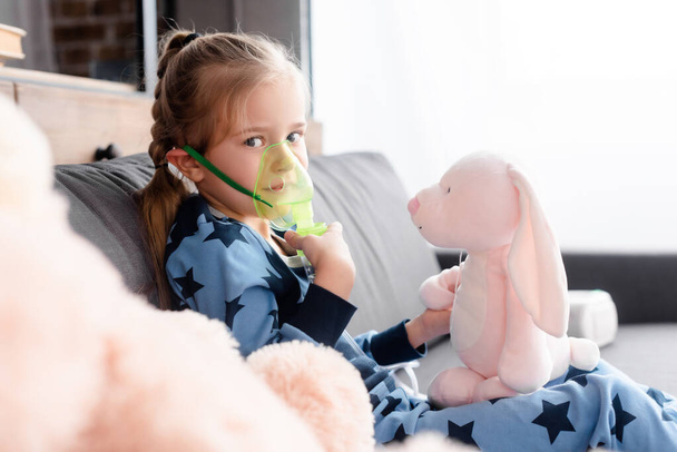 selektywne skupienie dziecka z astmą przy użyciu maski oddechowej w pobliżu miękkich zabawek  - Zdjęcie, obraz