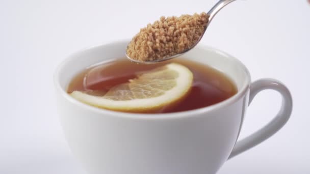 Bílý šálek s černým horkým čajem s plátkem citronu. Dezertní lžíce klade třtinový cukr a míchá nápoj. Vitamin Tonic - Záběry, video