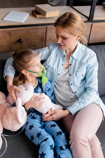 selektywne skupienie dziecka z astmą przy użyciu maski oddechowej i patrząc na miękką zabawkę w pobliżu matki  - Zdjęcie, obraz