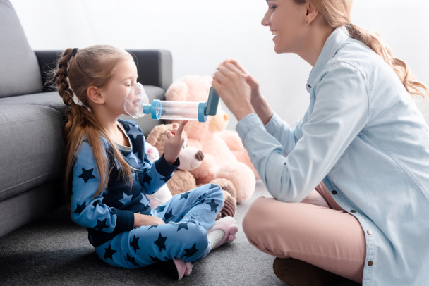 happy mother holding inhaler with spacer near sick kid  - Photo, Image