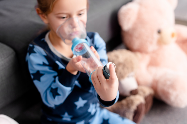 Selektive Fokussierung kranker Kinder durch Inhalator mit Abstandhalter in der Nähe von Stofftieren - Foto, Bild