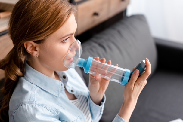 mujer asmática usando inhalador con espaciador en la sala de estar
  - Foto, imagen