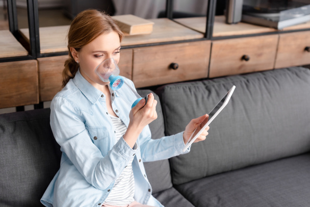 asthmatic woman using inhaler with spacer and holding digital tablet  - Photo, Image