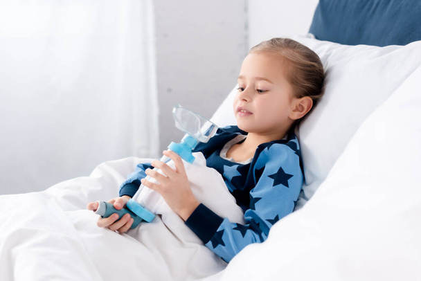 病気の子供がベッドルームに横たわっている間にスペーサーで吸入器を保持 - 写真・画像